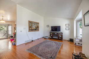 Living area with plenty of natural light, lofted ceiling, light wood-type flooring, and a chandelier