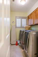Laundry room with a textured ceiling, light tile patterned floors, cabinet space, and separate washer and dryer
