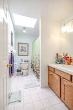 Bathroom with a skylight, vanity, light tile patterned flooring, and curtained shower