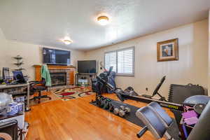 Exercise room featuring a brick fireplace, a textured ceiling, and wood finished floors