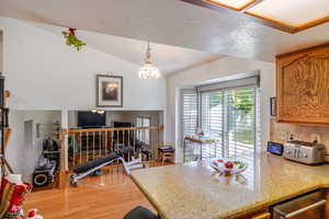 Kitchen featuring light wood finished floors, light stone counters, vaulted ceiling, decorative light fixtures, and a peninsula