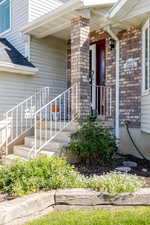 Property entrance featuring roof with shingles, a porch, and brick siding