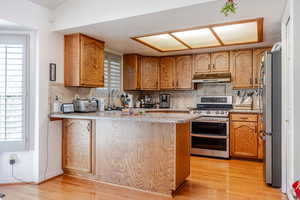 Kitchen with backsplash, stainless steel appliances, a peninsula, brown cabinetry, and light wood-type flooring