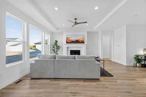 Living area featuring a raised ceiling, a fireplace, recessed lighting, light wood finished floors, and a ceiling fan