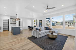 Living room featuring a tray ceiling, light wood-style floors, recessed lighting, ceiling fan, and a chandelier