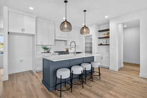 Kitchen with white cabinets, open shelves, a breakfast bar area, hanging light fixtures, and an island with sink