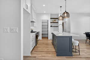 Kitchen featuring white cabinets, a breakfast bar, light stone counters, open shelves, and recessed lighting