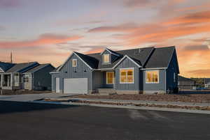 View of front facade featuring board and batten siding, driveway, a garage, and roof with shingles