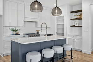 Kitchen with tasteful backsplash, a center island with sink, and white cabinets