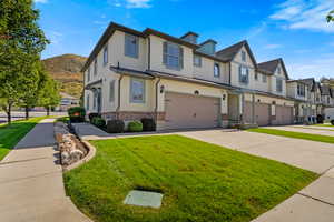 View of front facade featuring brick siding, stucco siding, a front lawn, concrete driveway, and a garage