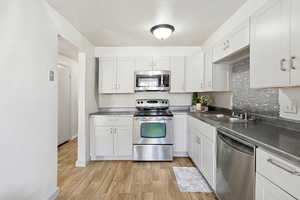 Kitchen with stainless steel countertops, appliances with stainless steel finishes, light wood-type flooring, and white cabinets