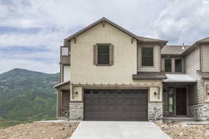 View of front of home featuring stone siding, an attached garage, concrete driveway, stucco siding, and a mountain view