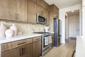 Kitchen featuring appliances with stainless steel finishes, tasteful backsplash, light wood-style floors, light stone countertops, and brown cabinets