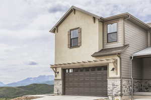 View of front facade featuring stone siding, an attached garage, a mountain view, and stucco siding