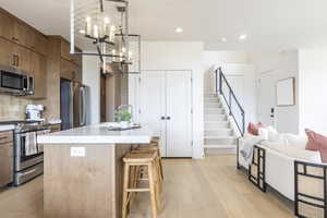 Kitchen featuring stainless steel appliances, a kitchen island with sink, light wood finished floors, tasteful backsplash, and decorative light fixtures