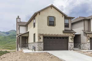 View of front facade featuring stone siding, stucco siding, an attached garage, concrete driveway, and a chimney