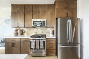 Kitchen with stainless steel appliances, decorative backsplash, and brown cabinetry