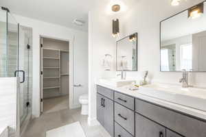 Bathroom featuring double vanity, a stall shower, a walk in closet, and light tile patterned floors