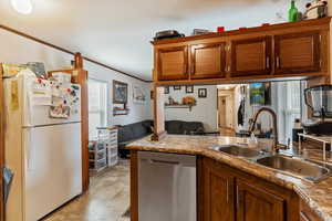 Kitchen with freestanding refrigerator, stainless steel dishwasher, brown cabinets, open floor plan, and ornamental molding