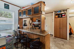 Kitchen featuring brown cabinetry, a breakfast bar, crown molding, glass insert cabinets, and a peninsula