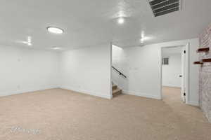 Finished below grade area with light carpet, a textured ceiling, and stairway