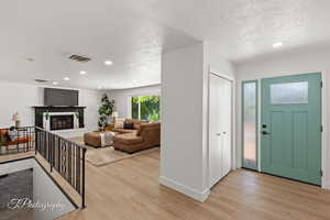 Foyer entrance featuring recessed lighting, light wood-style floors, a glass covered fireplace, and a textured ceiling