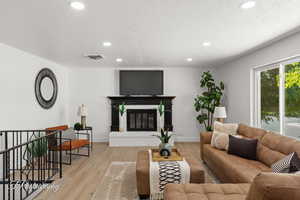 Living room featuring light wood finished floors, recessed lighting, a brick fireplace, and a textured ceiling