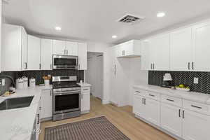 Kitchen featuring backsplash, light stone counters, stainless steel appliances, white cabinets, and recessed lighting