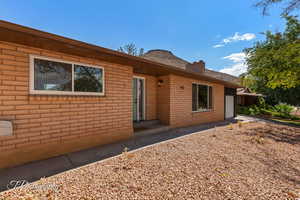 Back of house featuring brick siding, a chimney, a garage, and driveway