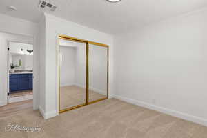 Unfurnished bedroom featuring a textured ceiling, light carpet, crown molding, and a closet