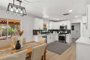 Kitchen featuring light stone counters, appliances with stainless steel finishes, light wood finished floors, tasteful backsplash, and white cabinetry