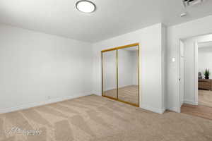 Unfurnished bedroom with light carpet, a closet, and a textured ceiling