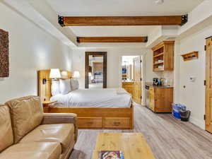 Bedroom featuring beam ceiling, light wood-type flooring, and ensuite bath