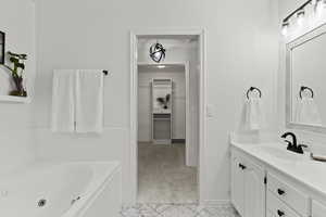 Full bathroom with vanity, a walk in closet, a jetted tub, light carpet, and light tile patterned floors