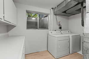 Laundry room featuring light wood-style floors, washer and clothes dryer, and cabinet space