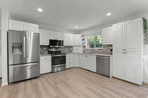 Kitchen with appliances with stainless steel finishes, white cabinets, light wood-type flooring, decorative backsplash, and open shelves
