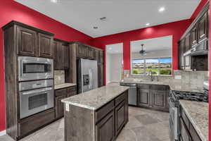 Kitchen featuring appliances with stainless steel finishes, backsplash, dark brown cabinets, under cabinet range hood, and a center island