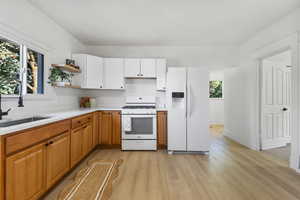 Kitchen with white appliances, brown cabinetry, light wood finished floors, open shelves, and white cabinetry