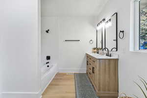 Full bathroom featuring double vanity, bathing tub / shower combination, light wood finished floors, and a textured ceiling