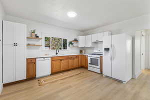 Kitchen with open shelves, white appliances, light countertops, and light wood-style flooring