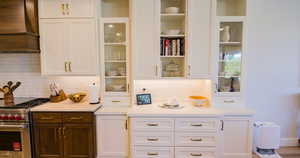 Kitchen with white cabinets, luxury range, custom range hood, and backsplash