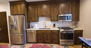 Kitchen featuring stainless steel appliances, tasteful backsplash, light wood finished floors, and light stone counters