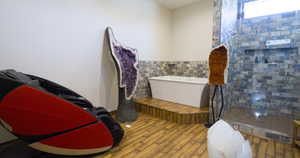 Bathroom with a soaking tub, a tile shower, wood finished floors, and tile walls