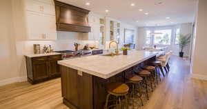 Kitchen featuring backsplash, a kitchen breakfast bar, glass insert cabinets, custom range hood, and white cabinets
