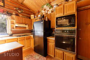 Kitchen with light wood finished floors, black appliances, light countertops, open shelves, and brown cabinetry