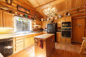 Kitchen with log walls, black appliances, light wood-style floors, decorative light fixtures, and a chandelier