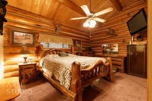 Carpeted bedroom with rustic walls, wood ceiling, and a ceiling fan