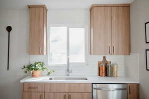 Kitchen with light brown cabinets, decorative backsplash, stainless steel dishwasher, and light stone counters