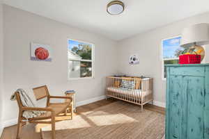 Bedroom featuring wood finished floors, multiple windows, and a crib