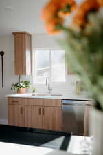 Kitchen featuring stainless steel dishwasher, backsplash, modern cabinets, and brown cabinetry
